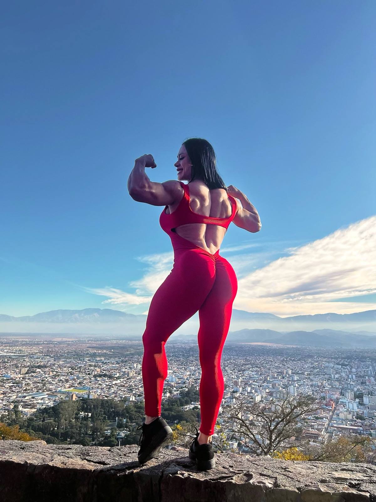 Roxana Palomo haciendo una pose de bíceps sobre el Cerro San Bernardo, con la ciudad de Salta de fondo